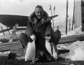 Photograph of Lincoln Ellsworth with two penguins in 1935. Snow and equipment are visible behind him.